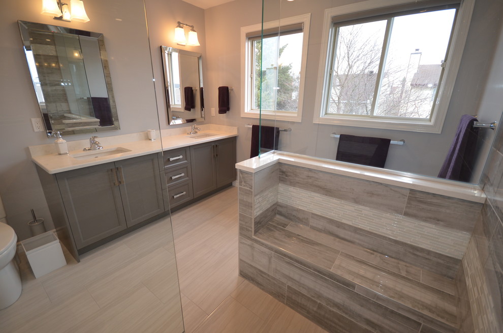 Inspiration for a contemporary ensuite half tiled bathroom in Ottawa with recessed-panel cabinets, grey cabinets, a built-in shower, a two-piece toilet, grey tiles, porcelain tiles, grey walls, porcelain flooring, a submerged sink, engineered stone worktops, beige floors and an open shower.