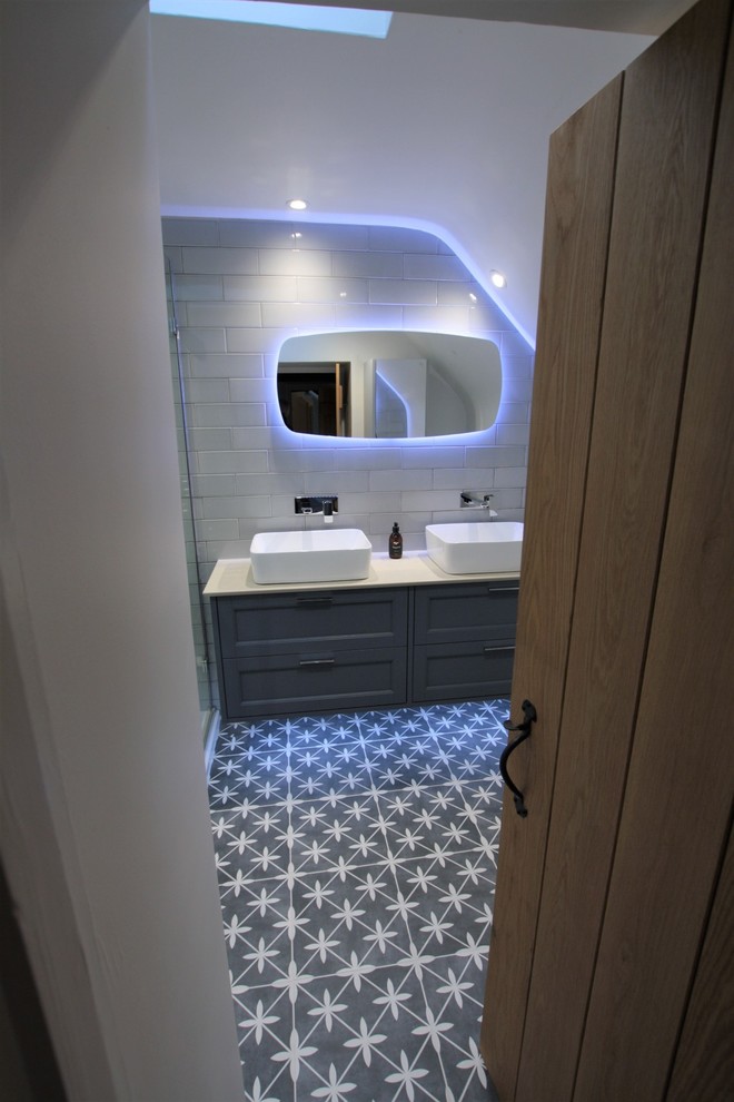 This is an example of a small contemporary ensuite bathroom in Oxfordshire with beaded cabinets, blue cabinets, a built-in shower, grey tiles, ceramic tiles, ceramic flooring, a vessel sink, solid surface worktops, grey floors, a hinged door and grey worktops.