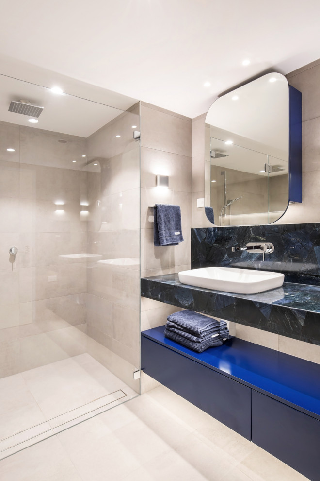 Inredning av ett modernt mellanstort blå blått en-suite badrum, med släta luckor, blå skåp, en dusch i en alkov, en vägghängd toalettstol, beige kakel, porslinskakel, beige väggar, klinkergolv i porslin, ett fristående handfat, beiget golv och dusch med gångjärnsdörr