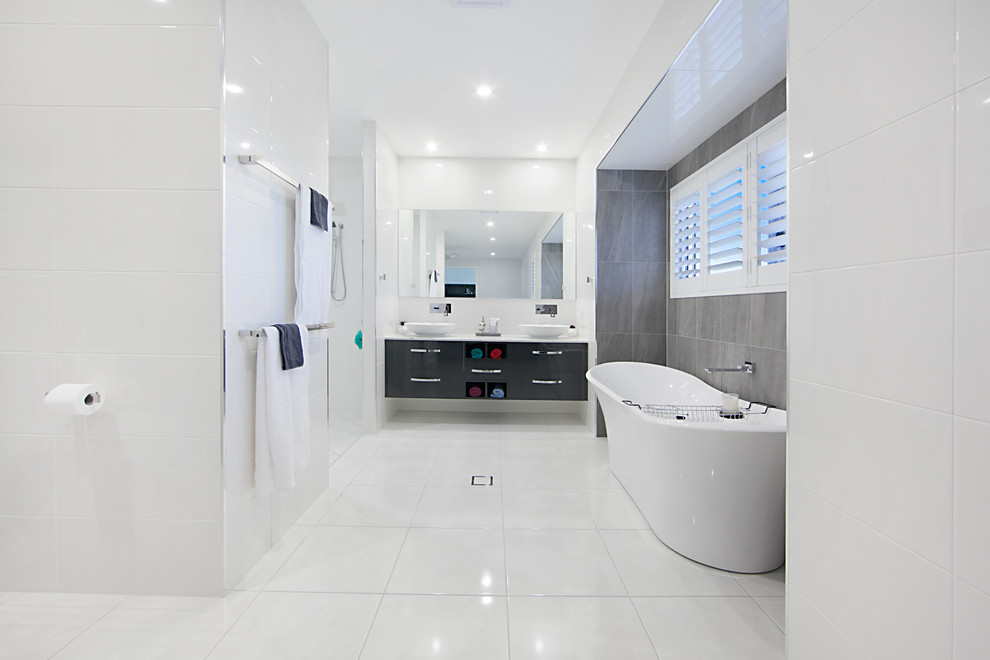 Großes Modernes Duschbad mit schwarzen Schränken, freistehender Badewanne, weißen Fliesen, Keramikfliesen, weißer Wandfarbe, Keramikboden, Aufsatzwaschbecken, weißem Boden, weißer Waschtischplatte, flächenbündigen Schrankfronten und Duschnische in Townsville