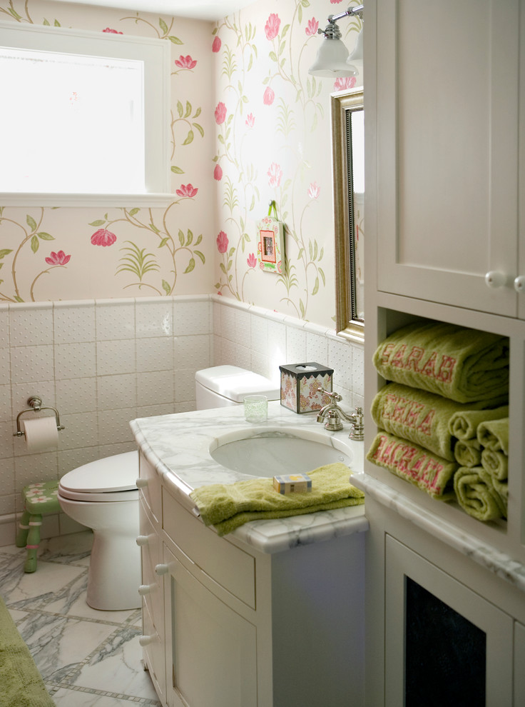 Klassisk inredning av ett badrum, med ett undermonterad handfat, vita skåp, marmorbänkskiva, vit kakel, porslinskakel och marmorgolv