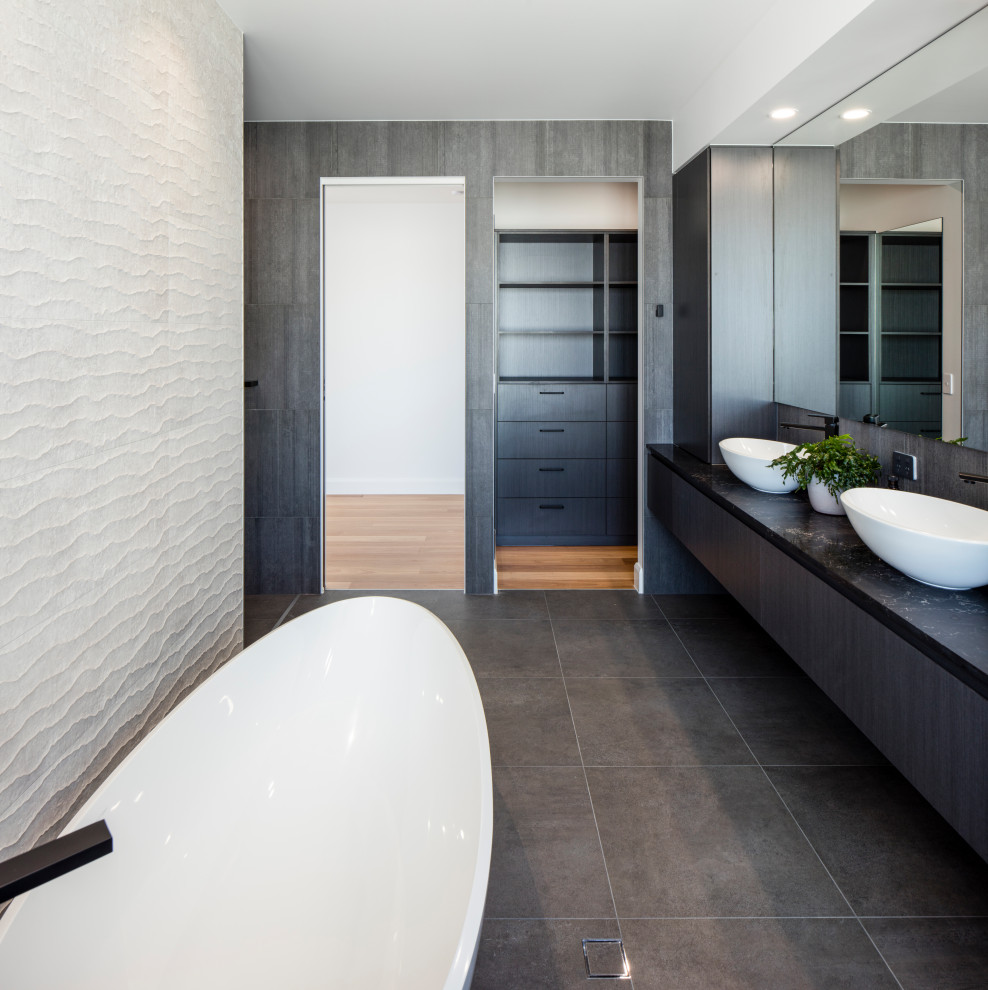 Idées déco pour une grande salle de bain principale contemporaine en bois foncé avec une baignoire indépendante, carreaux de ciment au sol, une vasque, un sol noir, un plan de toilette noir, meuble simple vasque, meuble-lavabo suspendu, un placard à porte plane et un carrelage gris.