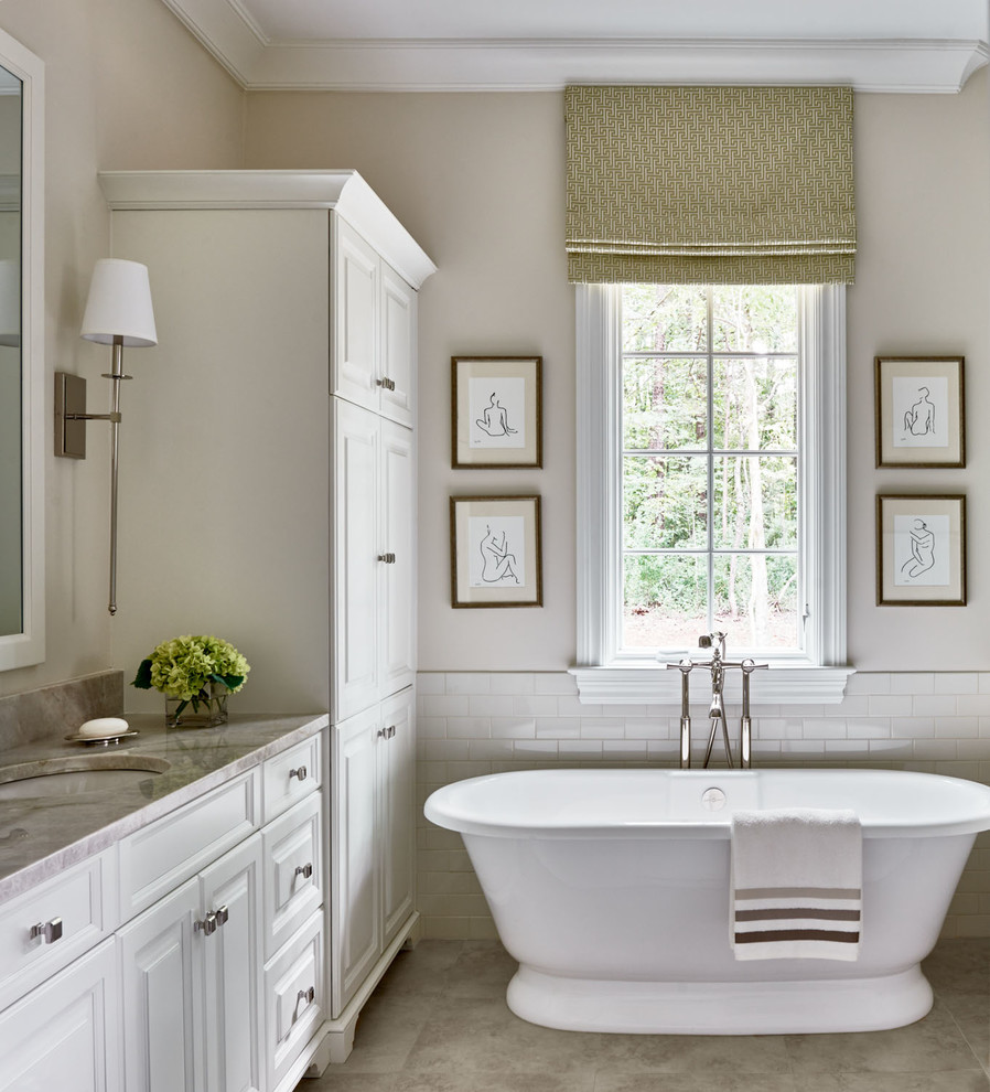 Foto på ett lantligt badrum, med ett undermonterad handfat, luckor med upphöjd panel, vita skåp, ett fristående badkar, vit kakel, tunnelbanekakel och beige väggar