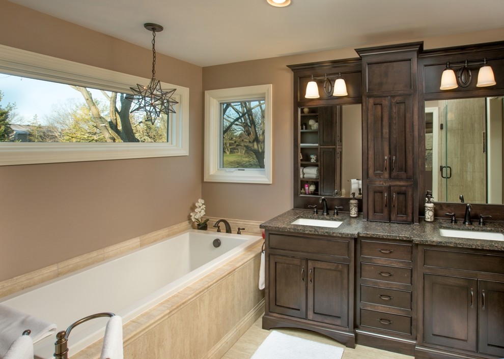 Klassisk inredning av ett badrum, med ett undermonterad handfat, skåp i shakerstil, skåp i mörkt trä, ett platsbyggt badkar och beige väggar