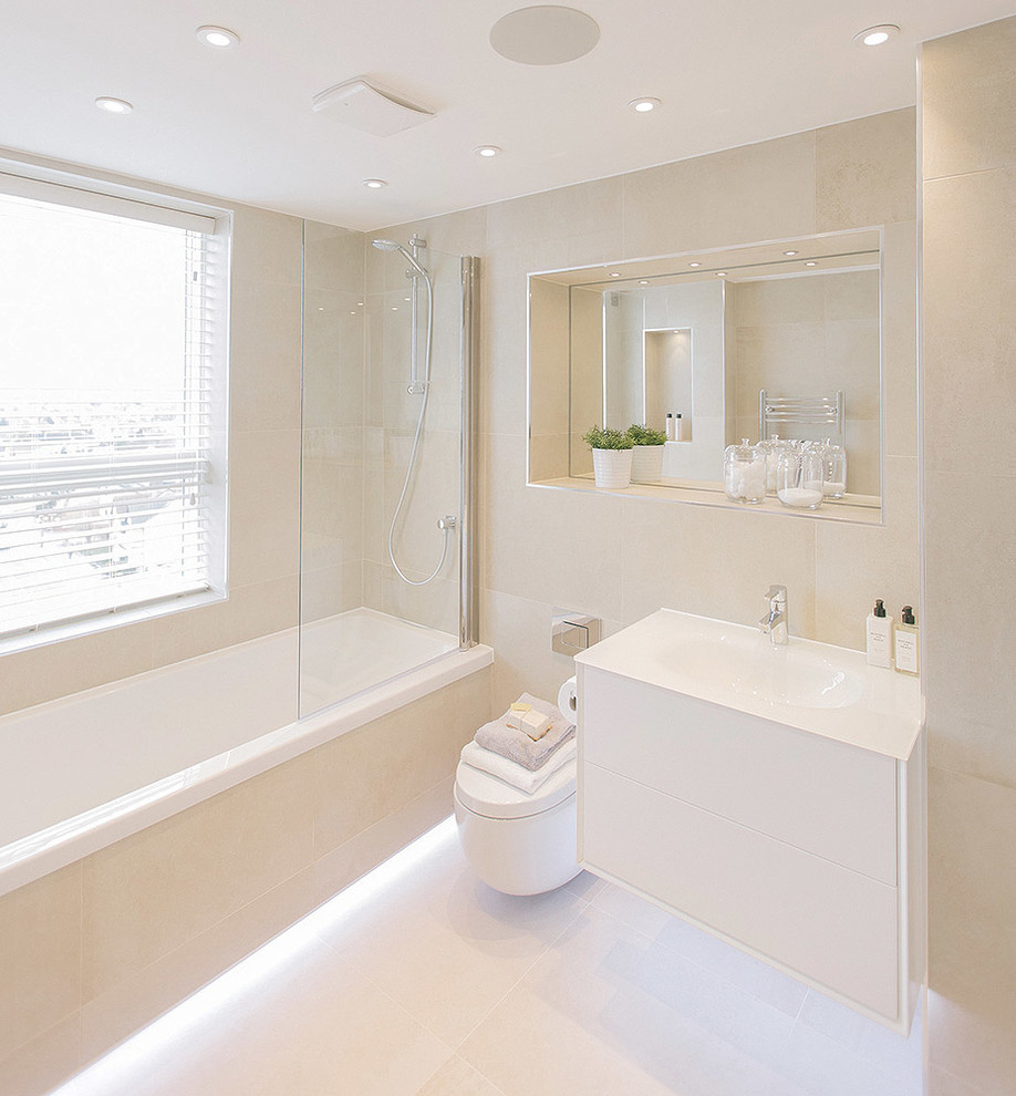 Inspiration for a medium sized contemporary family bathroom in London with white cabinets, a built-in bath, a shower/bath combination, a wall mounted toilet, white tiles, porcelain tiles, white walls, porcelain flooring, engineered stone worktops and an integrated sink.