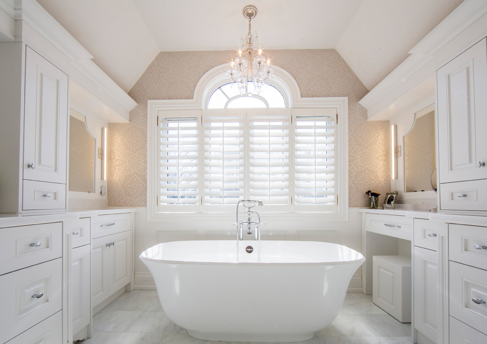 Foto på ett stort vintage en-suite badrum, med luckor med infälld panel, vita skåp, ett fristående badkar, en dusch i en alkov, en toalettstol med hel cisternkåpa, vit kakel, beige väggar, marmorgolv, ett undermonterad handfat och marmorbänkskiva