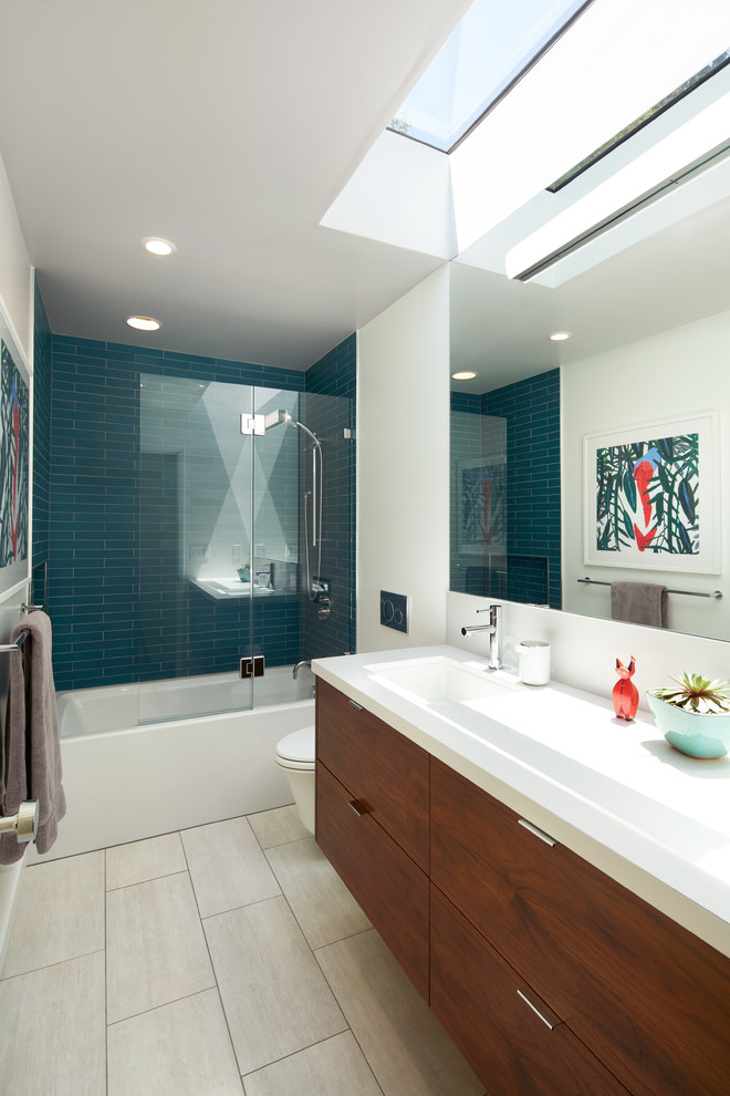 Стильный дизайн: маленькая ванная комната в стиле ретро с плоскими фасадами, фасадами цвета дерева среднего тона, ванной в нише, душем над ванной, унитазом-моноблоком, синей плиткой, плиткой из листового стекла, белыми стенами, полом из керамогранита, душевой кабиной, раковиной с несколькими смесителями, столешницей из искусственного кварца, бежевым полом, душем с распашными дверями и белой столешницей для на участке и в саду - последний тренд