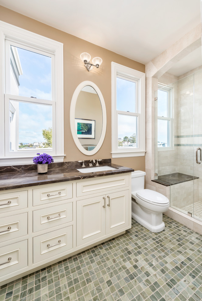 Photo of a large classic ensuite bathroom in San Francisco with a submerged sink, recessed-panel cabinets, white cabinets, an alcove shower, beige tiles, beige walls, mosaic tile flooring, a two-piece toilet, stone tiles and a shower bench.