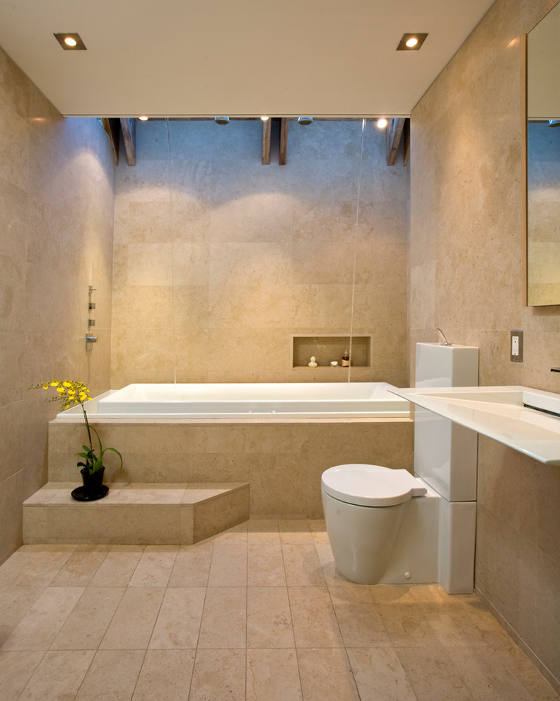 Idee per una stanza da bagno minimal con lavabo sospeso, vasca da incasso, vasca/doccia, WC a due pezzi e piastrelle beige