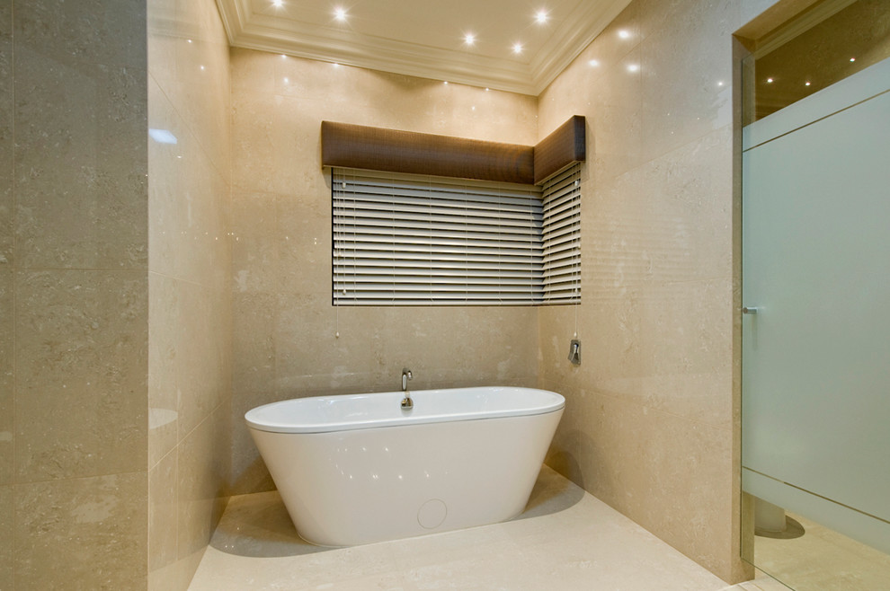 На фото: главная ванная комната среднего размера в современном стиле с отдельно стоящей ванной, унитазом-моноблоком, бежевой плиткой, керамогранитной плиткой, бежевыми стенами и полом из керамогранита с