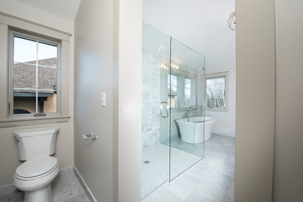 Klassisk inredning av ett stort en-suite badrum, med ett undermonterad handfat, möbel-liknande, grå skåp, granitbänkskiva, ett fristående badkar, en kantlös dusch, en toalettstol med separat cisternkåpa, vit kakel, grå väggar och marmorgolv
