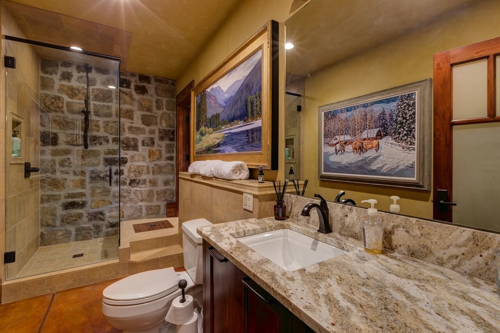 Exempel på ett mellanstort rustikt badrum med dusch, med skåp i shakerstil, skåp i mörkt trä, en dusch i en alkov, en toalettstol med separat cisternkåpa, stenkakel, gula väggar, betonggolv, ett undermonterad handfat, granitbänkskiva, med dusch som är öppen och brunt golv