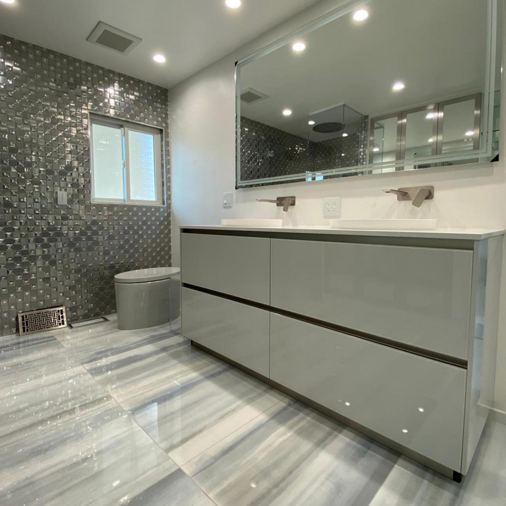 This is an example of a medium sized contemporary ensuite bathroom in San Diego with glass-front cabinets, grey cabinets, a corner shower, white tiles, glass sheet walls, grey walls, ceramic flooring, terrazzo worktops, grey floors, a hinged door, grey worktops, an enclosed toilet, double sinks, a freestanding vanity unit, a coffered ceiling and panelled walls.