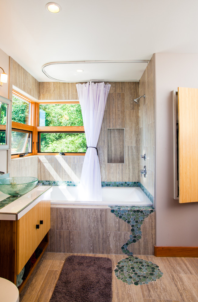 Photo of a contemporary bathroom in Seattle with a vessel sink, flat-panel cabinets, medium wood cabinets, a built-in bath, a shower/bath combination, multi-coloured tiles, pebble tiles and beige walls.