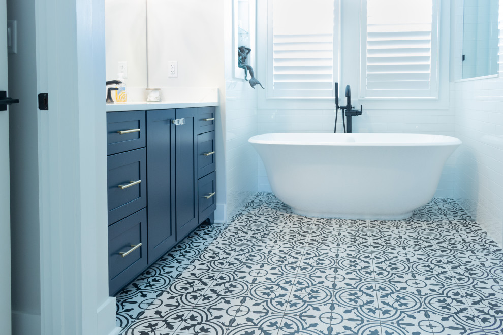 Freestanding bathtub - transitional porcelain tile, multicolored floor and single-sink freestanding bathtub idea in Jacksonville with shaker cabinets, blue cabinets, white walls, solid surface countertops, white countertops and a built-in vanity
