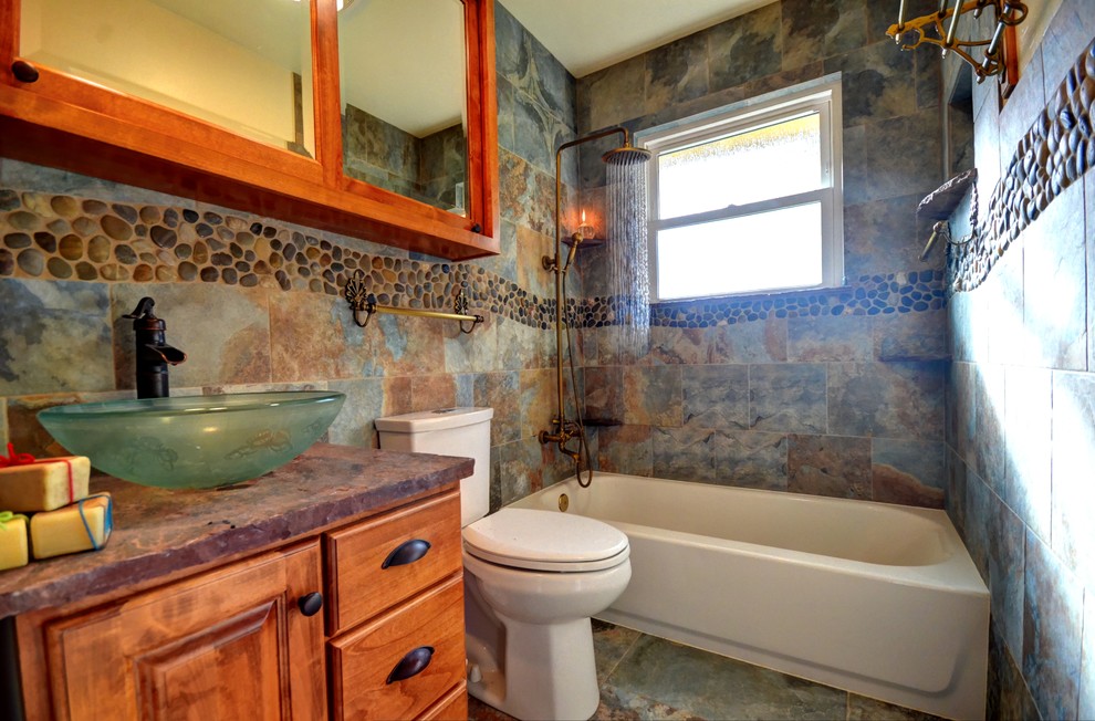 Foto på ett lantligt badrum, med luckor med upphöjd panel, skåp i mellenmörkt trä, ett platsbyggt badkar, grå kakel, stenhäll, ett fristående handfat och marmorbänkskiva