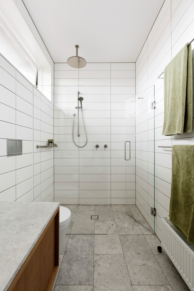 Inredning av ett retro vit vitt badrum, med vit kakel, marmorbänkskiva, släta luckor, skåp i mellenmörkt trä, en dusch i en alkov, grått golv och dusch med gångjärnsdörr
