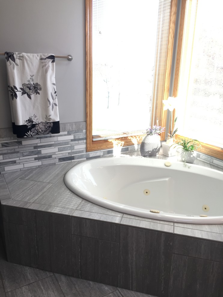 Expansive classic ensuite wet room bathroom in Omaha with raised-panel cabinets, medium wood cabinets, a built-in bath, a two-piece toilet, grey tiles, ceramic tiles, grey walls, ceramic flooring, a submerged sink, quartz worktops, grey floors, a hinged door and white worktops.