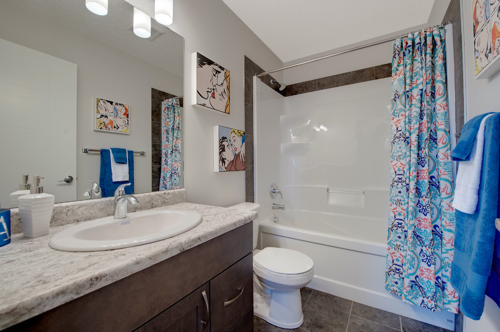 Cette image montre une petite douche en alcôve principale design avec un placard avec porte à panneau surélevé, des portes de placard grises, une baignoire en alcôve, WC à poser, un carrelage gris, un mur blanc, un lavabo posé et un plan de toilette en stratifié.