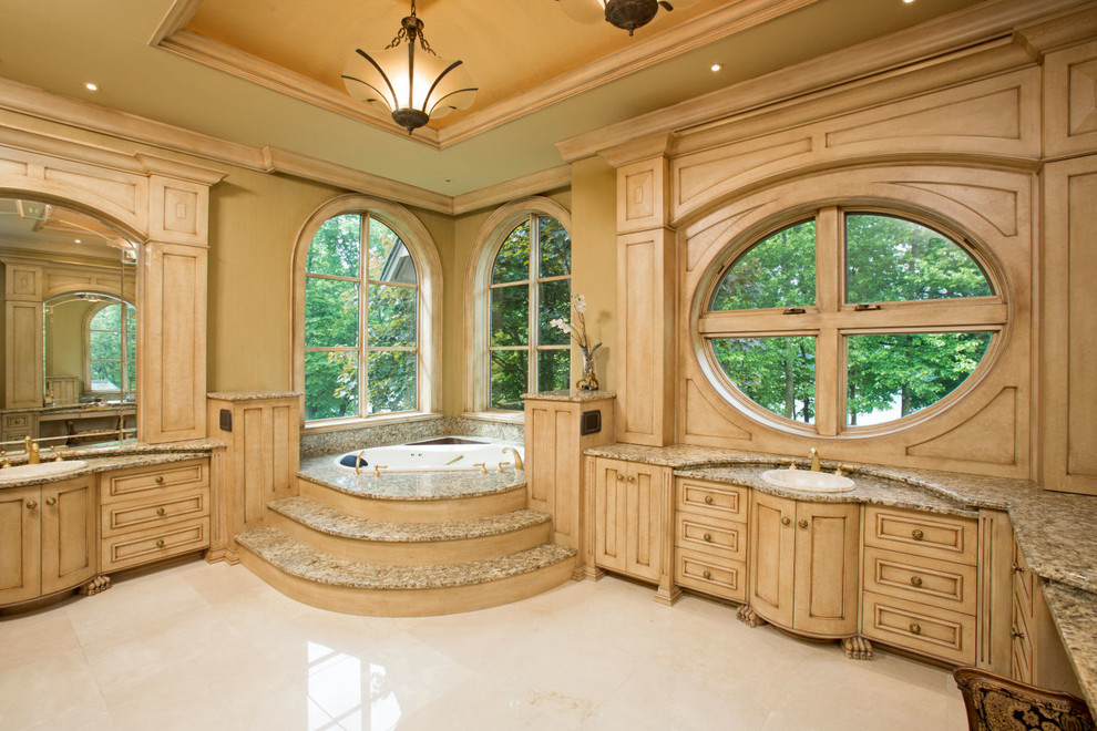 Modelo de cuarto de baño principal clásico con puertas de armario de madera clara, bañera esquinera, lavabo encastrado y armarios con paneles empotrados