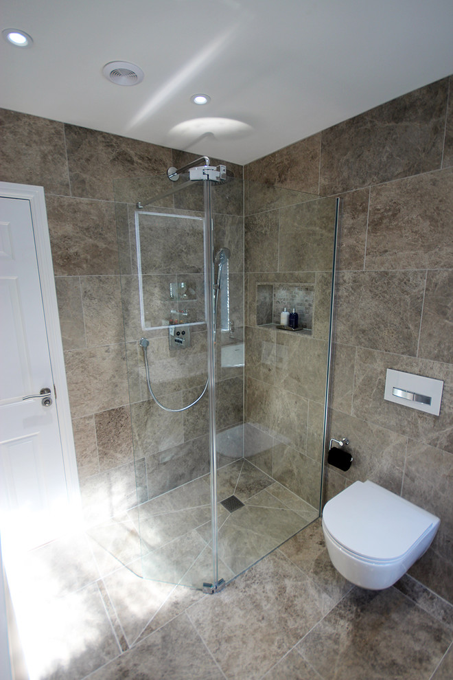 Cette photo montre une grande salle de bain principale tendance avec un placard à porte plane, des portes de placard grises, une baignoire indépendante, un espace douche bain, WC suspendus, un carrelage gris, un carrelage de pierre, un mur gris, un sol en calcaire, un lavabo suspendu et un sol gris.