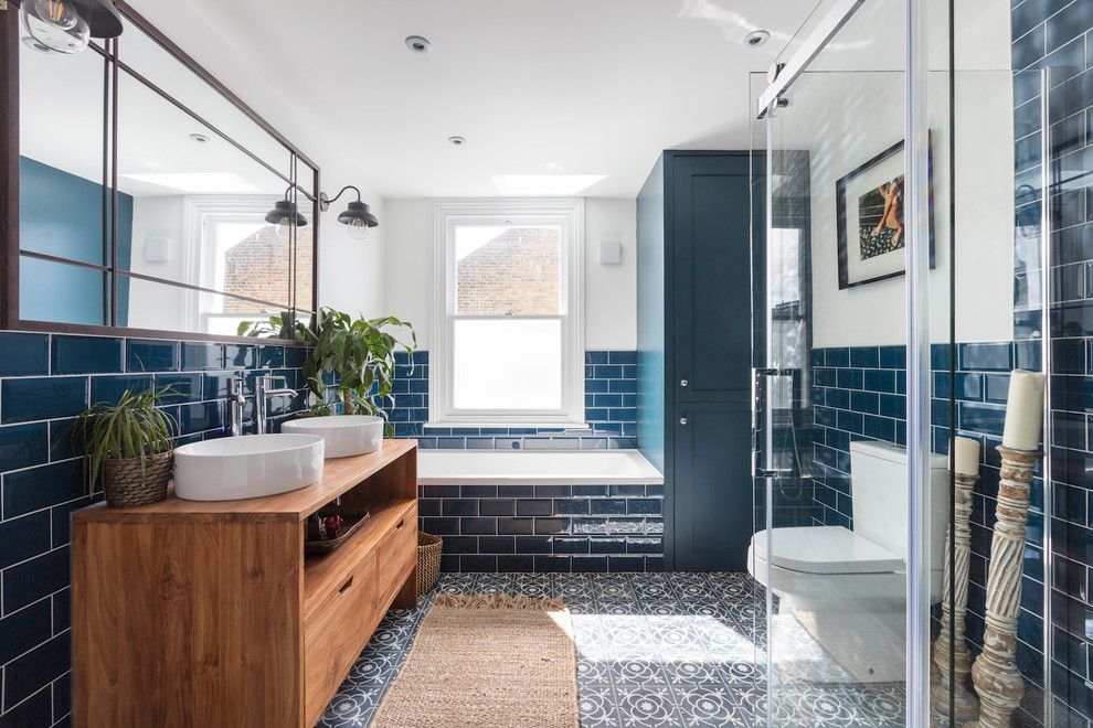 ロンドンにある中くらいなトランジショナルスタイルのおしゃれな子供用バスルーム (フラットパネル扉のキャビネット、中間色木目調キャビネット、ドロップイン型浴槽、コーナー設置型シャワー、分離型トイレ、青いタイル、サブウェイタイル、白い壁、セメントタイルの床、ベッセル式洗面器、木製洗面台、マルチカラーの床、ブラウンの洗面カウンター) の写真