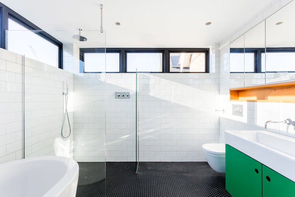 This is an example of a large modern bathroom in London with flat-panel cabinets, green cabinets, a freestanding bath, white tiles, ceramic tiles, white walls, mosaic tile flooring, black floors and an open shower.