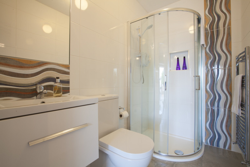 Badezimmer mit weißen Schränken, Eckdusche, Wandtoilette mit Spülkasten, orangen Fliesen, bunten Wänden und Schiebetür-Duschabtrennung in Cork