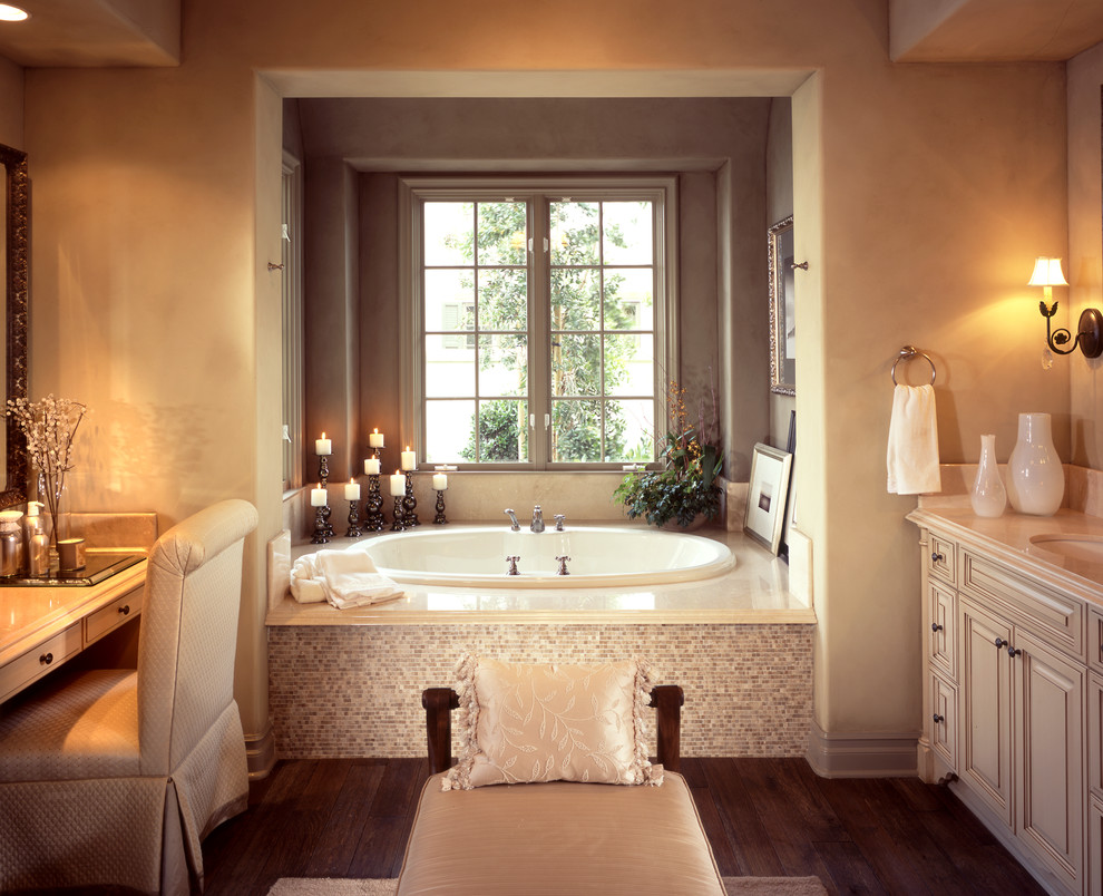 Exempel på ett mellanstort klassiskt en-suite badrum, med luckor med upphöjd panel, beige skåp, ett platsbyggt badkar, beige kakel, glaskakel, beige väggar, mörkt trägolv, ett undermonterad handfat, laminatbänkskiva och brunt golv