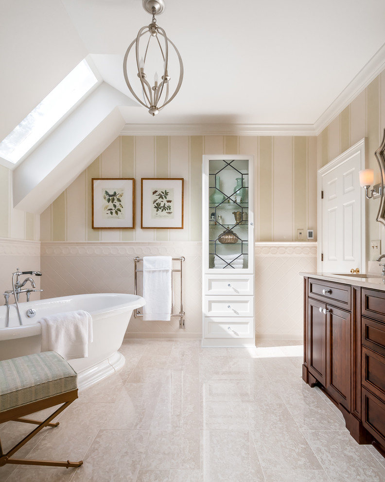 Пример оригинального дизайна: ванная комната в классическом стиле с темными деревянными фасадами, отдельно стоящей ванной, бежевой плиткой, бежевыми стенами, врезной раковиной, бежевым полом и фасадами с декоративным кантом