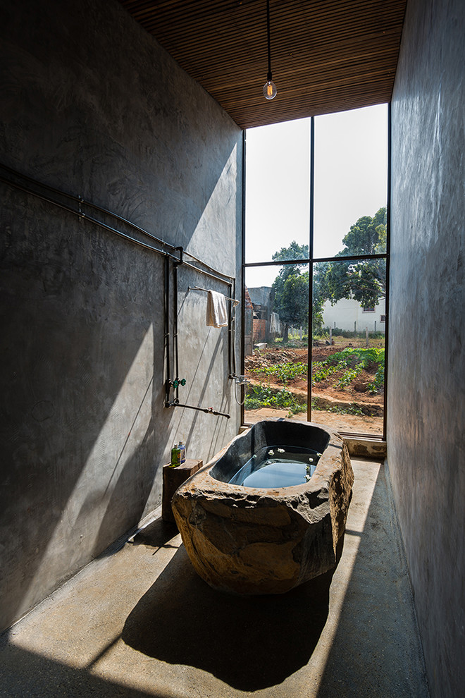 Cette photo montre une salle de bain principale industrielle avec une baignoire indépendante, un mur gris, sol en béton ciré et un sol gris.