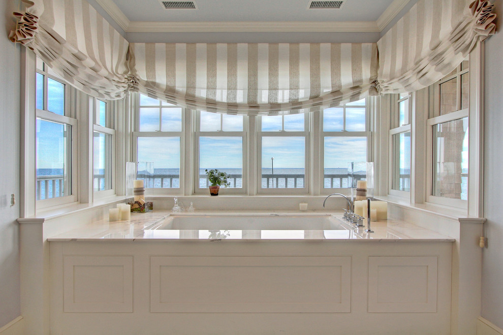 Diseño de cuarto de baño principal marinero de tamaño medio con lavabo integrado, armarios con paneles con relieve, puertas de armario blancas, encimera de mármol, bañera encastrada, paredes grises y suelo de mármol