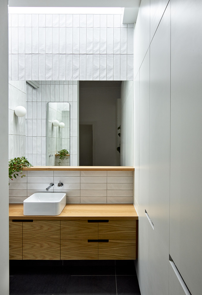 Modern inredning av ett litet brun brunt en-suite badrum, med släta luckor, skåp i ljust trä, vit kakel, keramikplattor, vita väggar, klinkergolv i porslin, ett fristående handfat, träbänkskiva och grått golv