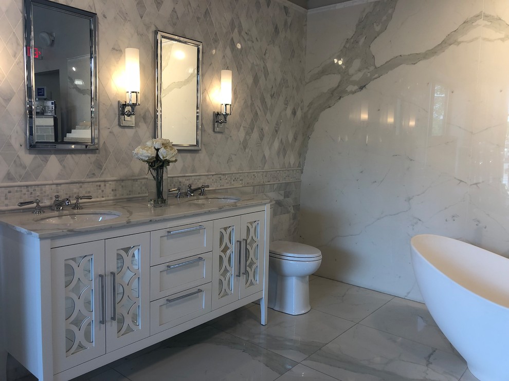 Inredning av ett klassiskt mellanstort vit vitt en-suite badrum, med luckor med glaspanel, vita skåp, ett fristående badkar, en toalettstol med separat cisternkåpa, grå kakel, stenhäll, vita väggar, marmorgolv, ett undermonterad handfat, bänkskiva i kvarts och grått golv