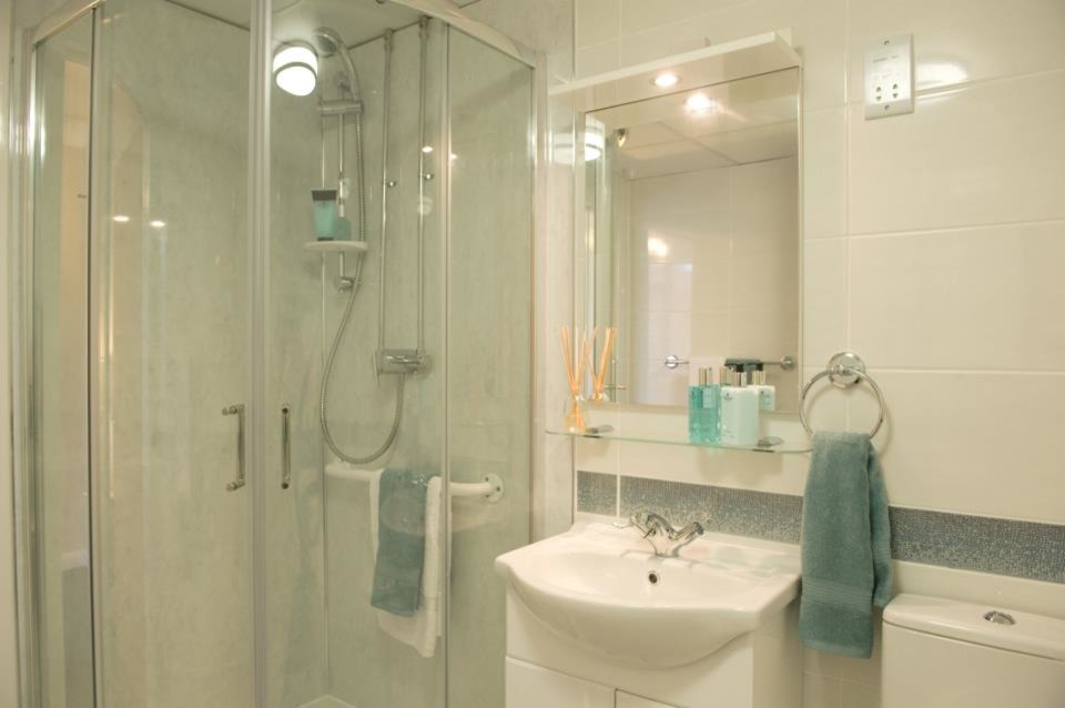 This is an example of a small contemporary shower room bathroom in Dorset with a console sink, freestanding cabinets, white cabinets, laminate worktops, a corner shower, a two-piece toilet, white tiles, ceramic tiles, white walls and vinyl flooring.