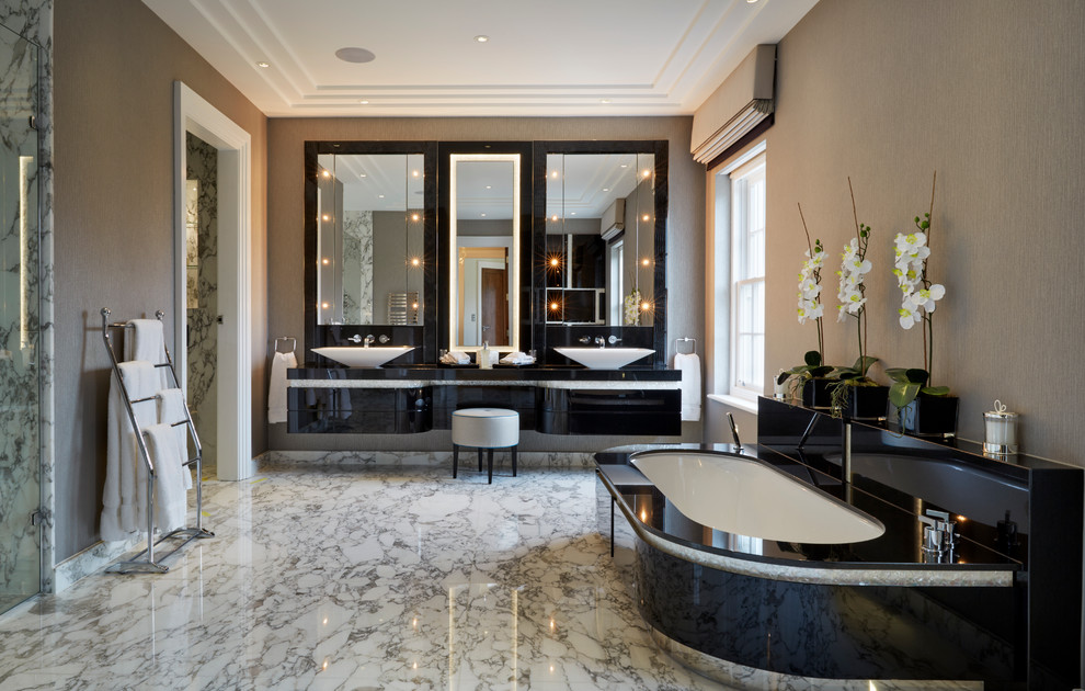 Modern inredning av ett en-suite badrum, med ett fristående handfat, släta luckor, svarta skåp, ett undermonterat badkar och beige väggar