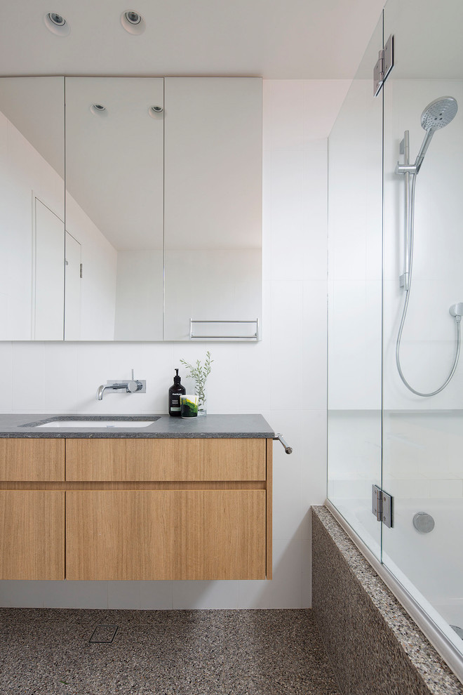 Inspiration for a medium sized contemporary ensuite bathroom in Sydney with flat-panel cabinets, medium wood cabinets, a built-in bath, a shower/bath combination, a one-piece toilet, white tiles, porcelain tiles, white walls, terracotta flooring, a submerged sink, engineered stone worktops, brown floors, a hinged door and grey worktops.