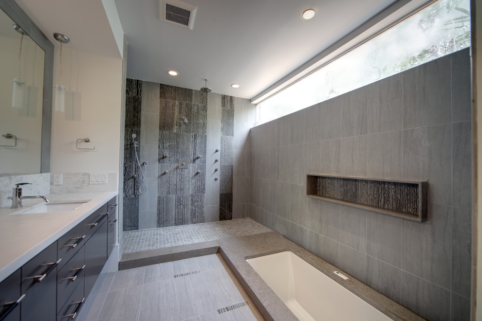 Large modern ensuite bathroom in Houston with a submerged sink, a submerged bath, a walk-in shower, an open shower, flat-panel cabinets, black cabinets, grey tiles, stone tiles, porcelain flooring, engineered stone worktops and grey floors.