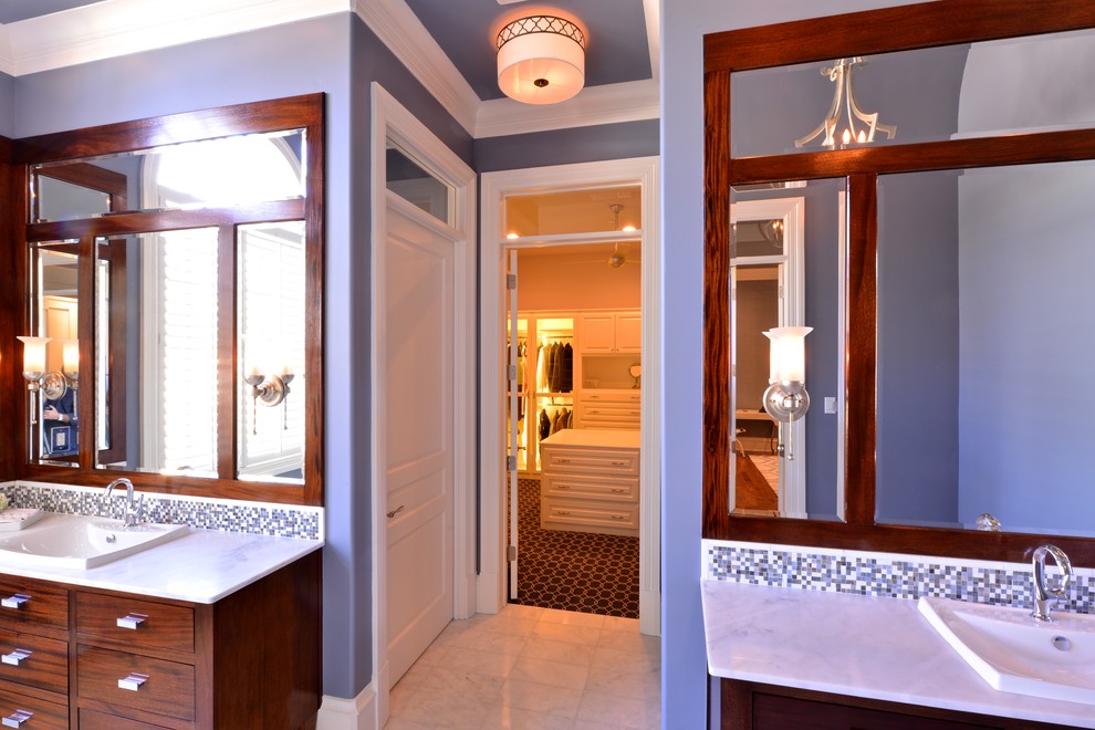 Klassisk inredning av ett stort badrum, med ett nedsänkt handfat, släta luckor, skåp i mörkt trä, marmorbänkskiva, ett fristående badkar, en toalettstol med hel cisternkåpa, vit kakel, grå väggar och marmorgolv