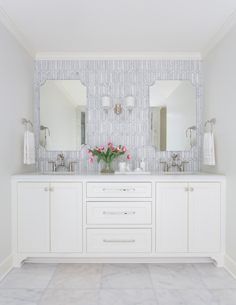 Klassisk inredning av ett vit vitt badrum, med luckor med infälld panel, vita skåp, grå kakel, marmorkakel, vita väggar, ett undermonterad handfat och vitt golv