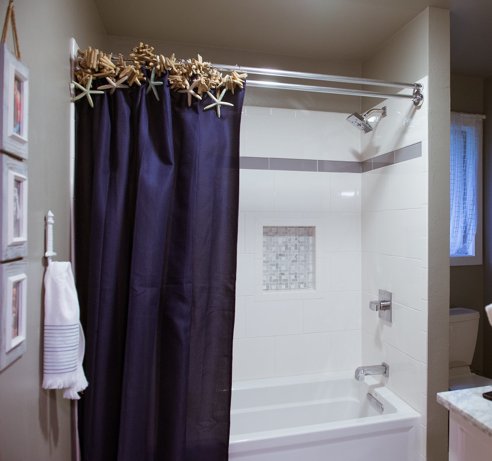 This is an example of a small beach style family bathroom in Seattle with white cabinets, beaded cabinets, an alcove bath, a shower/bath combination, a one-piece toilet, beige tiles, ceramic tiles, beige walls, porcelain flooring, a submerged sink, marble worktops, grey floors and a shower curtain.