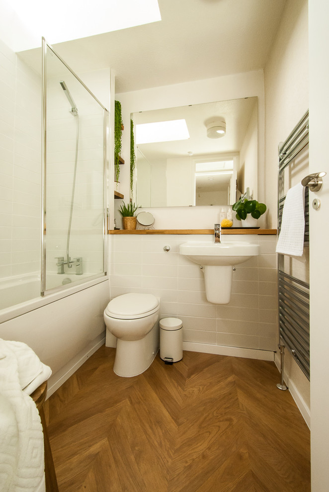 Small contemporary family bathroom in Other with open cabinets, light wood cabinets, a built-in bath, a shower/bath combination, a one-piece toilet, white tiles, ceramic tiles, beige walls, light hardwood flooring, a wall-mounted sink, wooden worktops, brown floors, a hinged door and brown worktops.