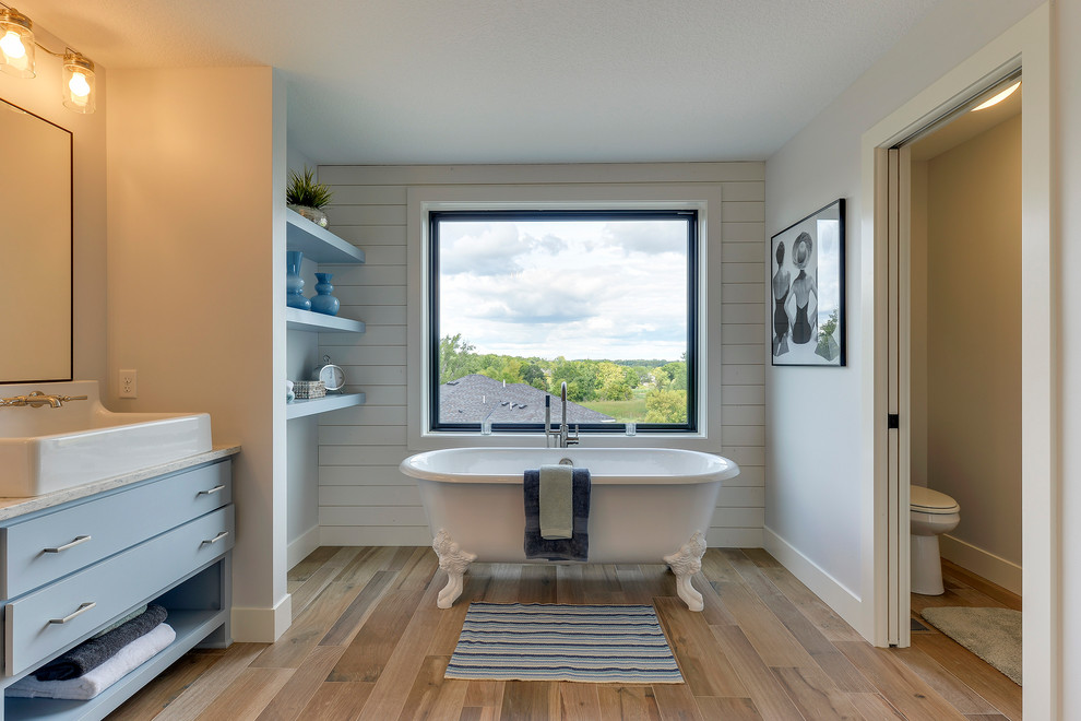 Inspiration for a medium sized rural ensuite bathroom in Minneapolis with blue cabinets, a claw-foot bath, a walk-in shower, a one-piece toilet, porcelain flooring, a trough sink, marble worktops, brown floors, an open shower, flat-panel cabinets, blue walls and an enclosed toilet.