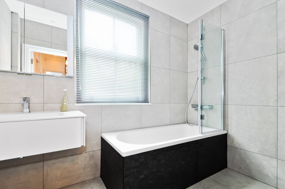 Ejemplo de cuarto de baño contemporáneo con lavabo suspendido, armarios con paneles lisos, bañera esquinera, ducha abierta, sanitario de pared, baldosas y/o azulejos grises y baldosas y/o azulejos de porcelana
