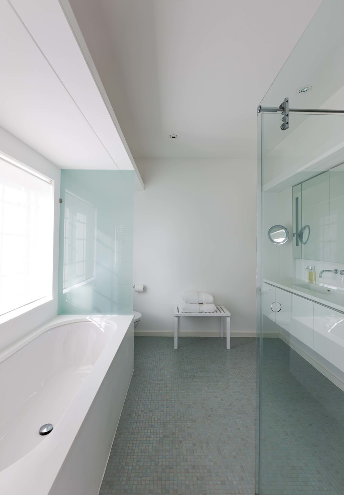 Immagine di una stanza da bagno moderna con ante lisce, ante bianche, doccia aperta, WC sospeso, pareti bianche, pavimento con piastrelle a mosaico, lavabo sottopiano, top in superficie solida, pavimento verde, porta doccia scorrevole e top bianco