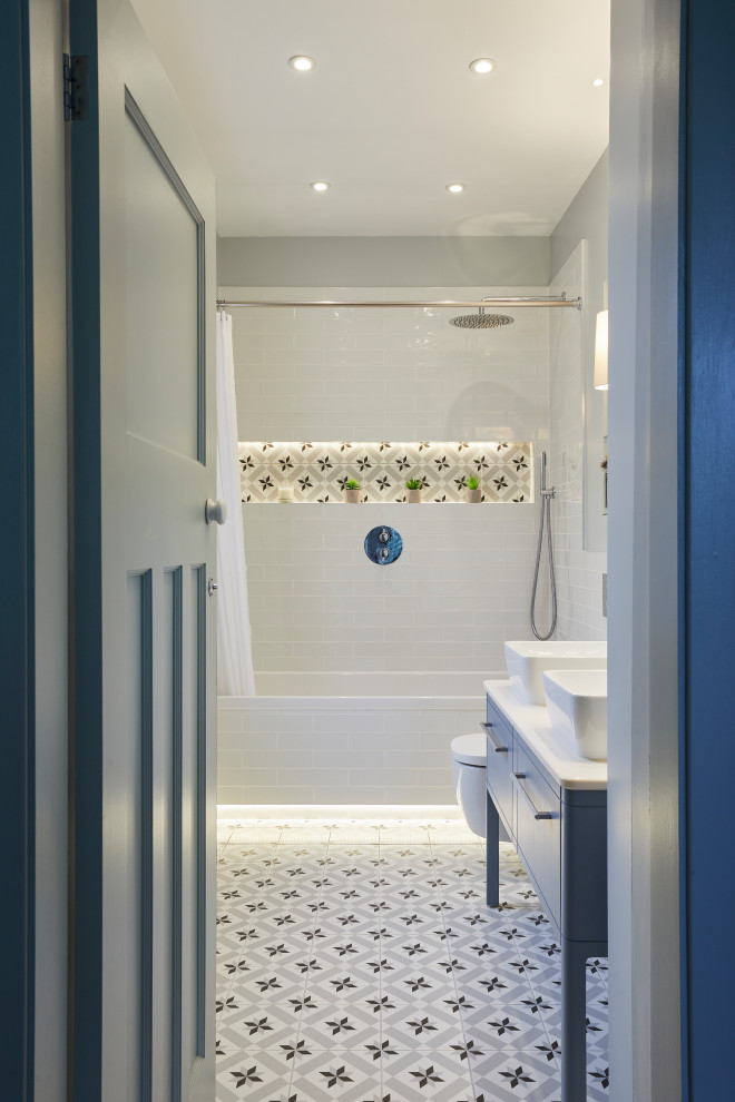 Пример оригинального дизайна: ванная комната в современном стиле с синими фасадами, накладной ванной, душем над ванной, инсталляцией, белой плиткой, керамической плиткой, синими стенами, полом из керамической плитки, раковиной с пьедесталом, разноцветным полом, шторкой для ванной, белой столешницей и тумбой под две раковины