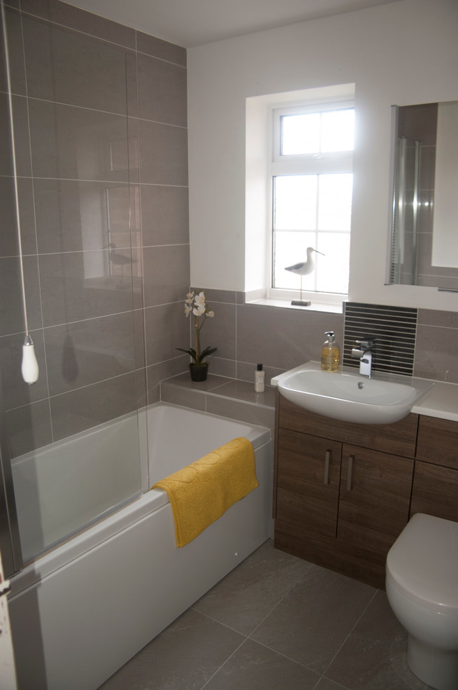 This is an example of a medium sized contemporary bathroom in Berkshire with a built-in sink, medium wood cabinets, solid surface worktops, a shower/bath combination, grey tiles, porcelain tiles and grey walls.