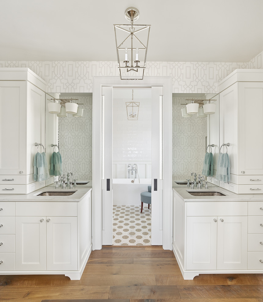 Example of a large beach style master white tile beige floor and medium tone wood floor bathroom design in Charleston with white walls, a hinged shower door, recessed-panel cabinets, white cabinets, an undermount sink, quartzite countertops and gray countertops