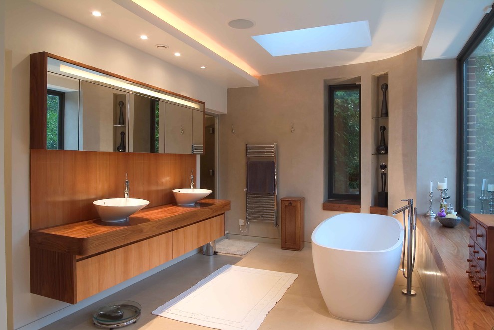 Freestanding bathtub - contemporary freestanding bathtub idea in London with a vessel sink, flat-panel cabinets, medium tone wood cabinets, wood countertops and beige walls