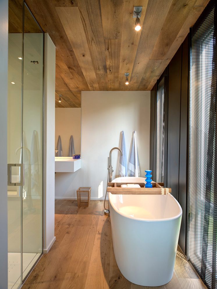 Cette photo montre une salle de bain tendance avec une baignoire indépendante, un mur blanc et un sol en bois brun.